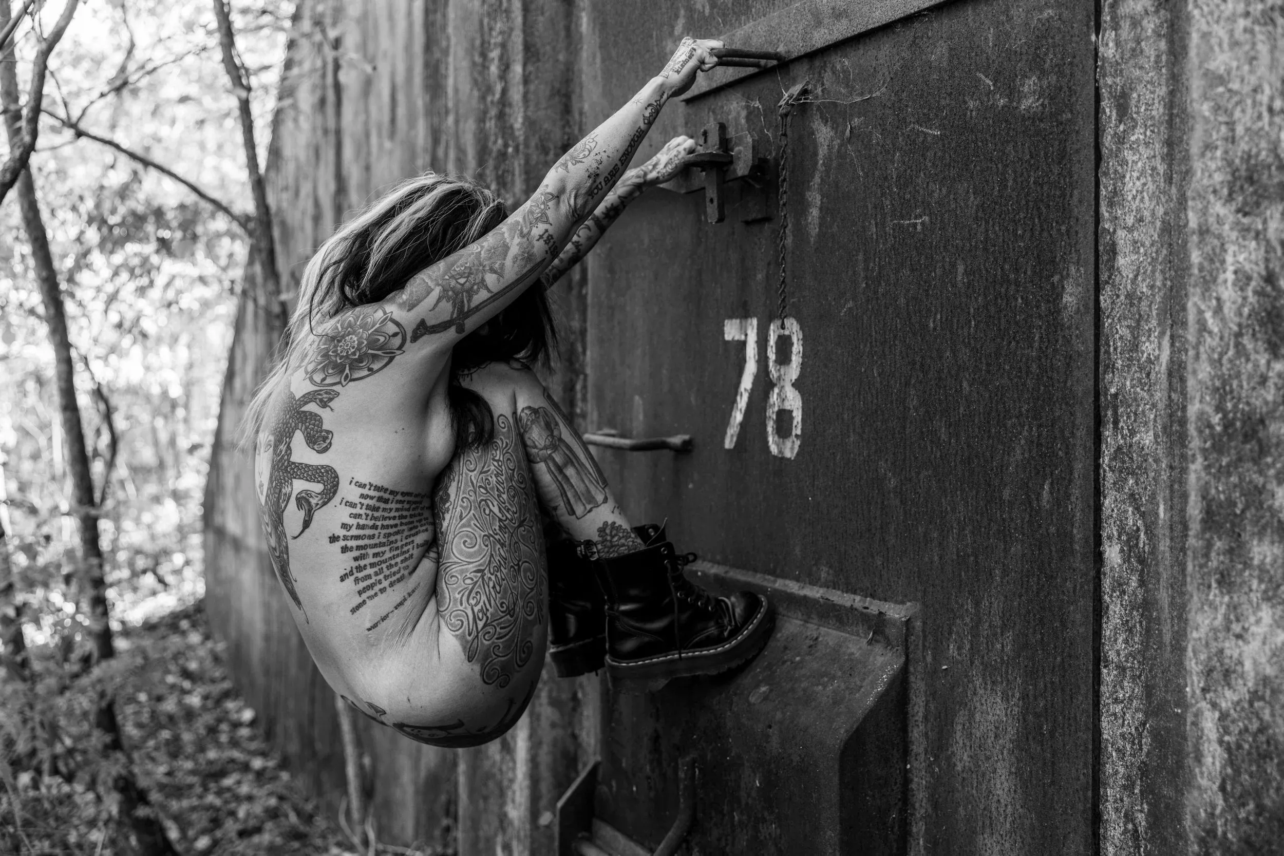 A tattooed woman climbs the heavy metal door of Bunker 78.
