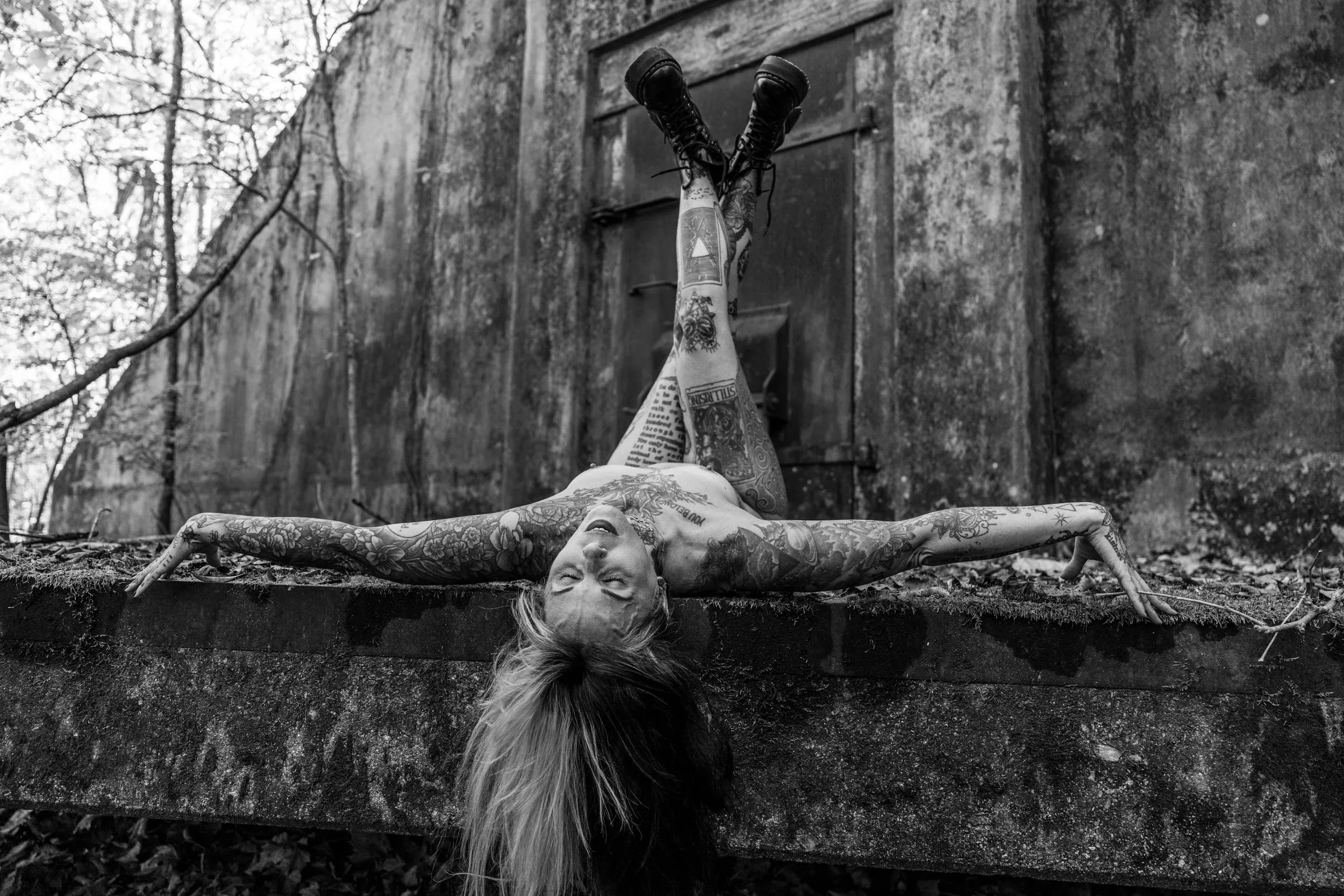 A woman hangs upside down from a rusted beam in the forest.