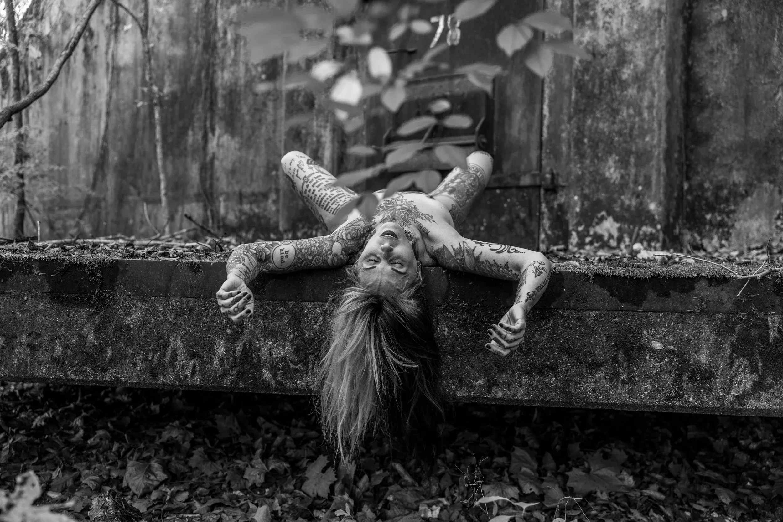 A tattooed figure arches over a weathered concrete wall.