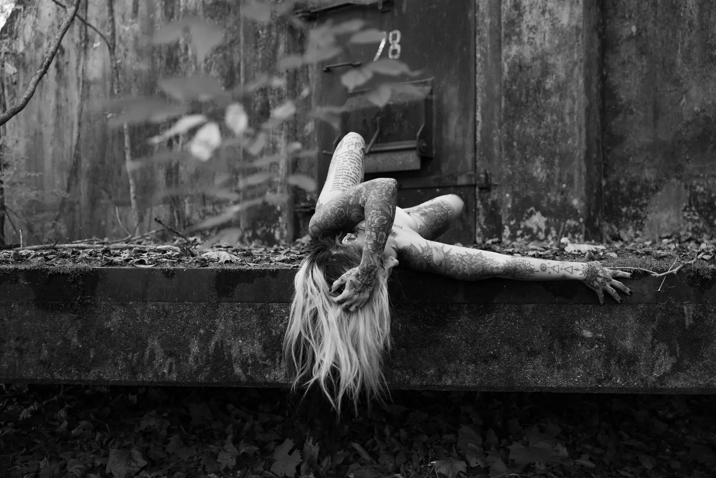 A woman hangs headfirst across a ledge as leaves blur the foreground.