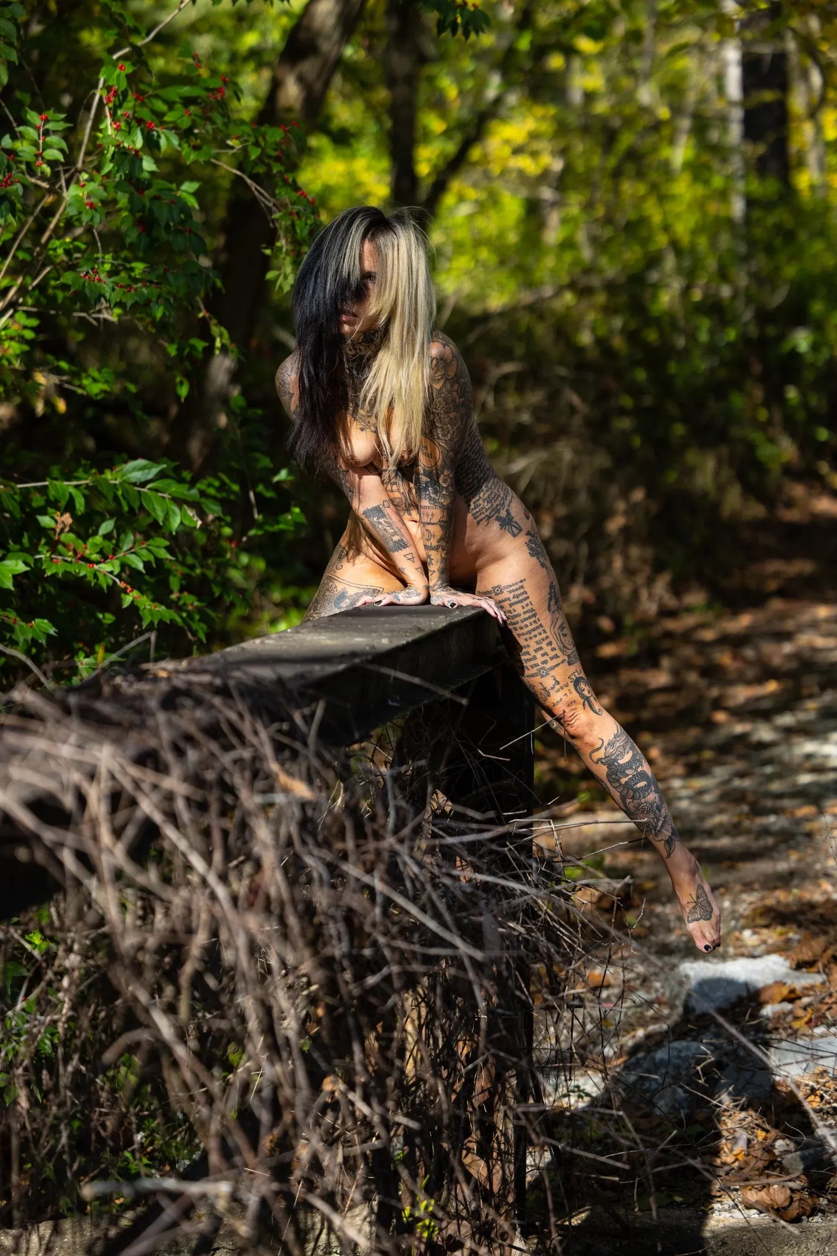A woman sits on the root ball of a fallen tree in green woodland.