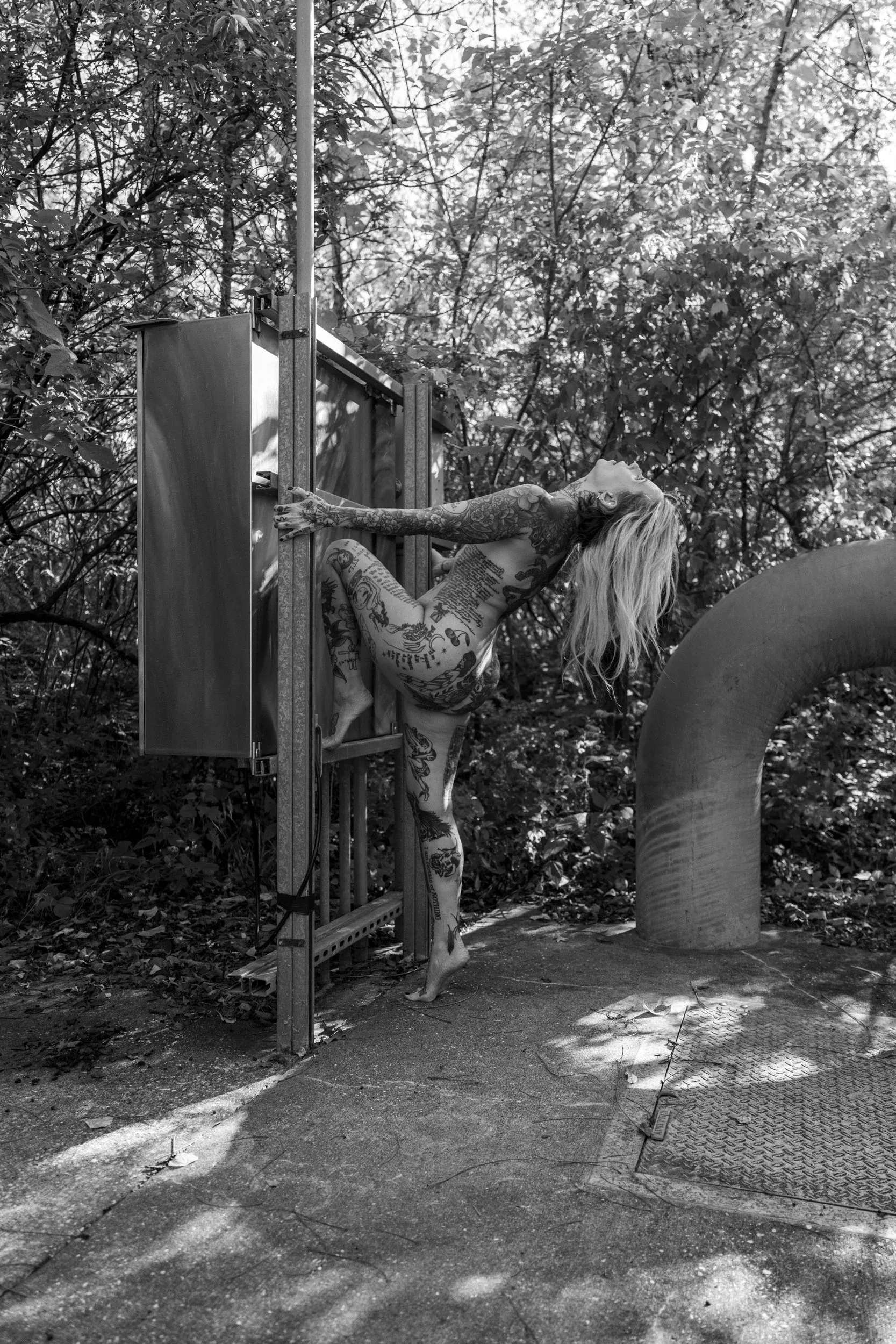 A woman leans from a metal structure beside a large curved pipe.