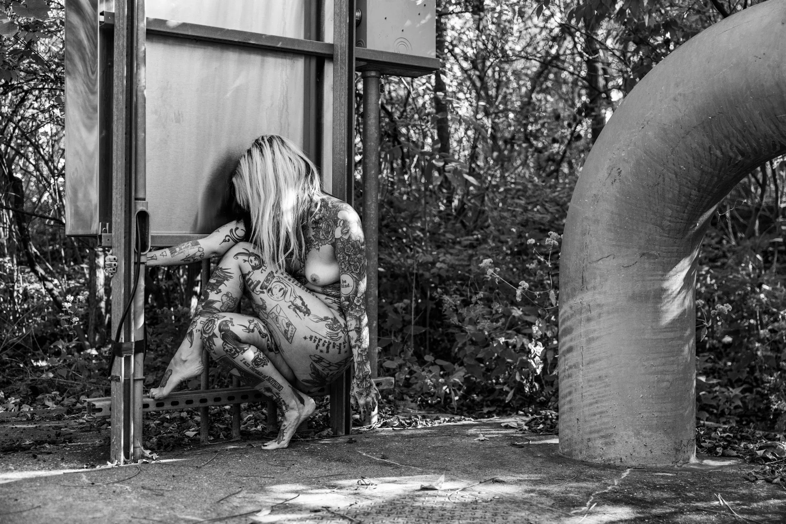A tattooed woman crouches in the doorway of weathered machinery.