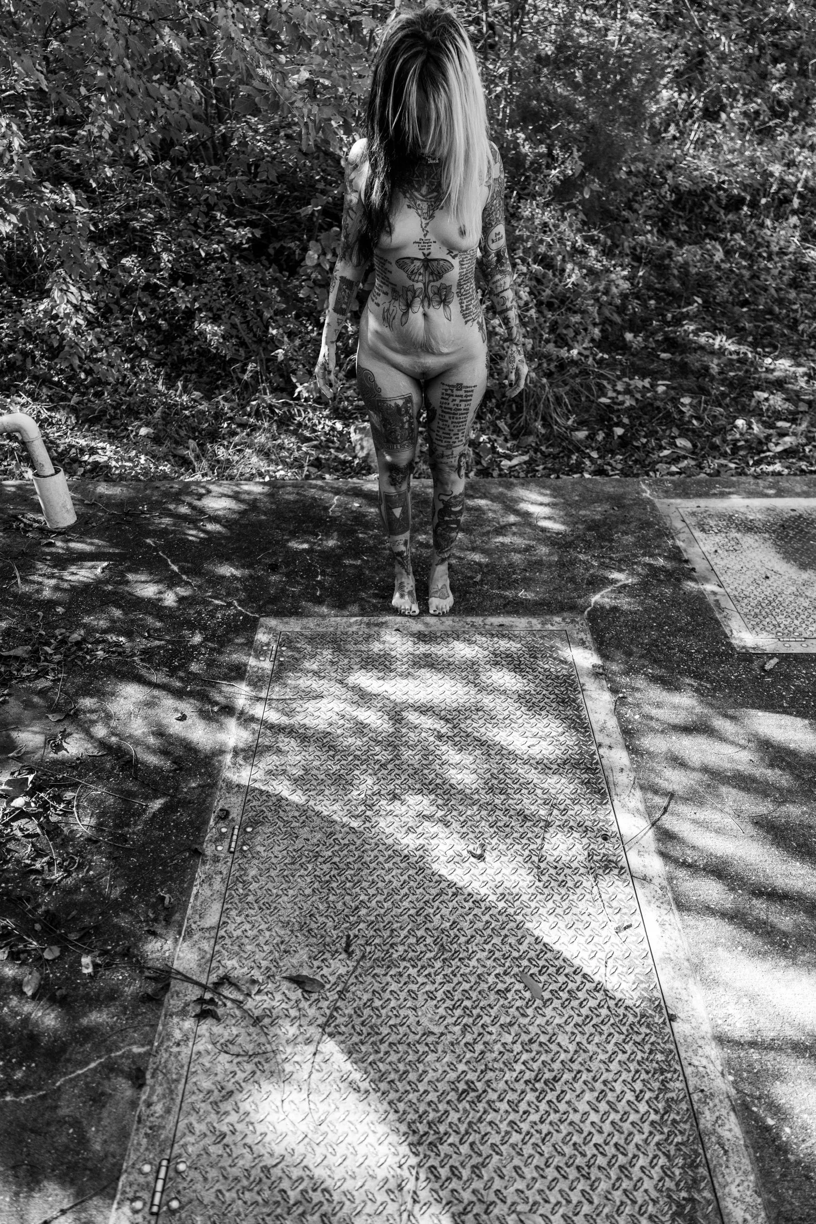 A woman walks away along a sun-dappled concrete path in the woods.