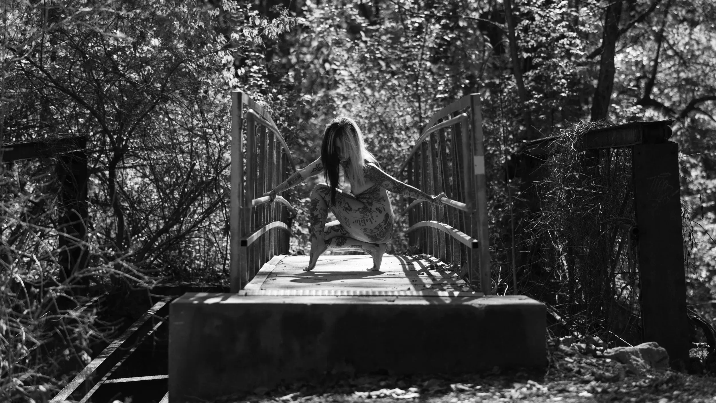 A woman balances on an abandoned bridge between trees.