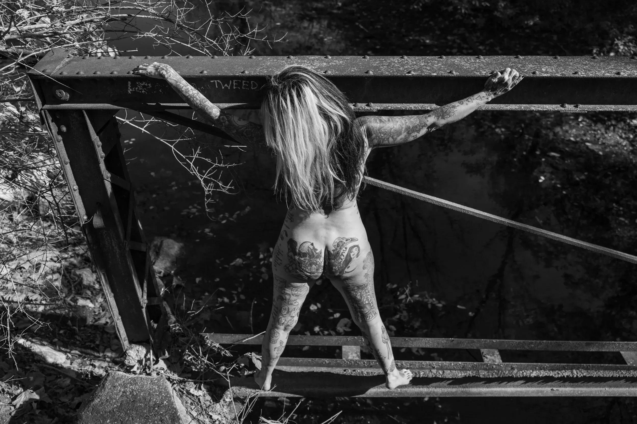A tattooed woman stretches across a rusted outdoor structure.