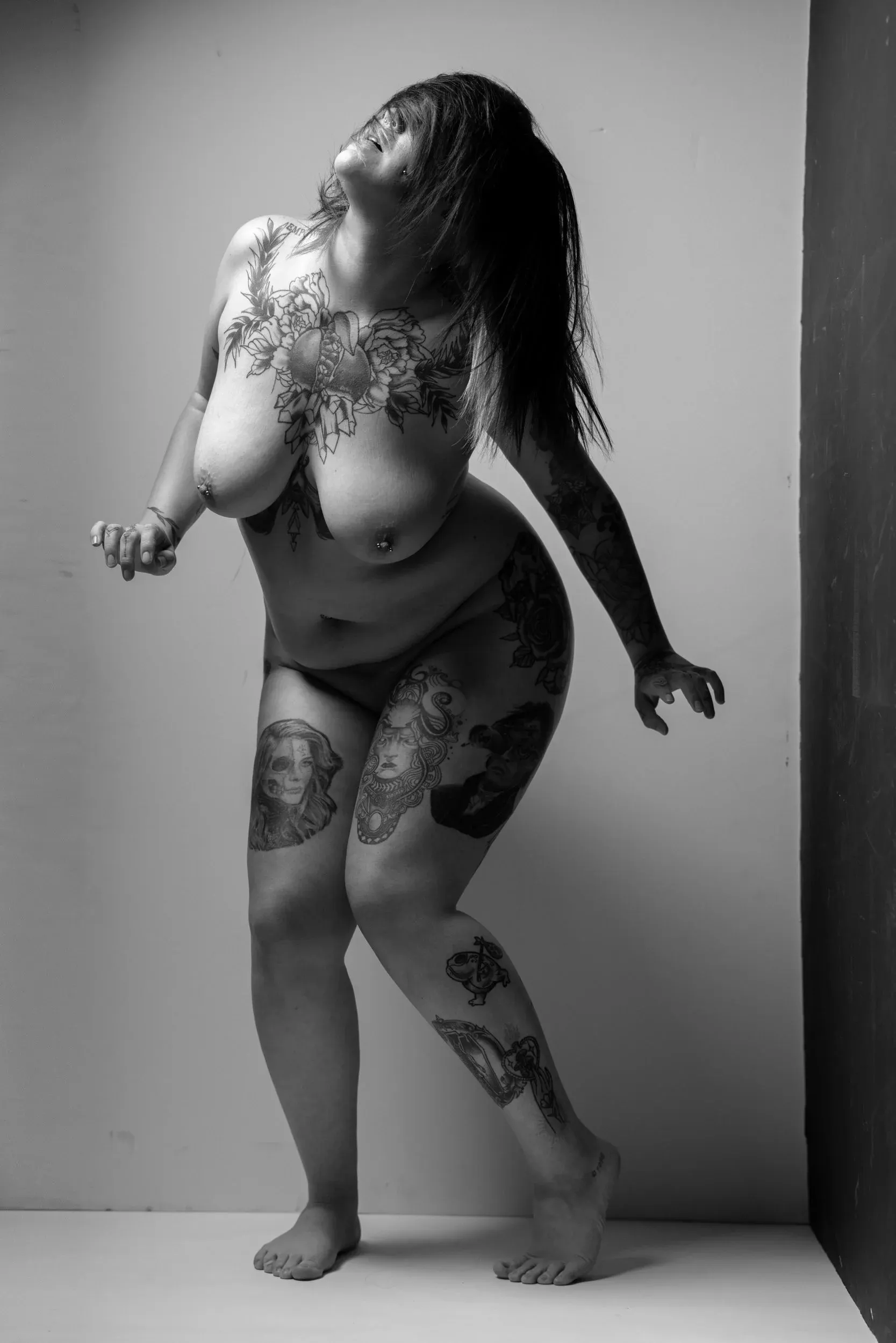 A standing woman leans forward as her hair and tattoos form dark shapes.