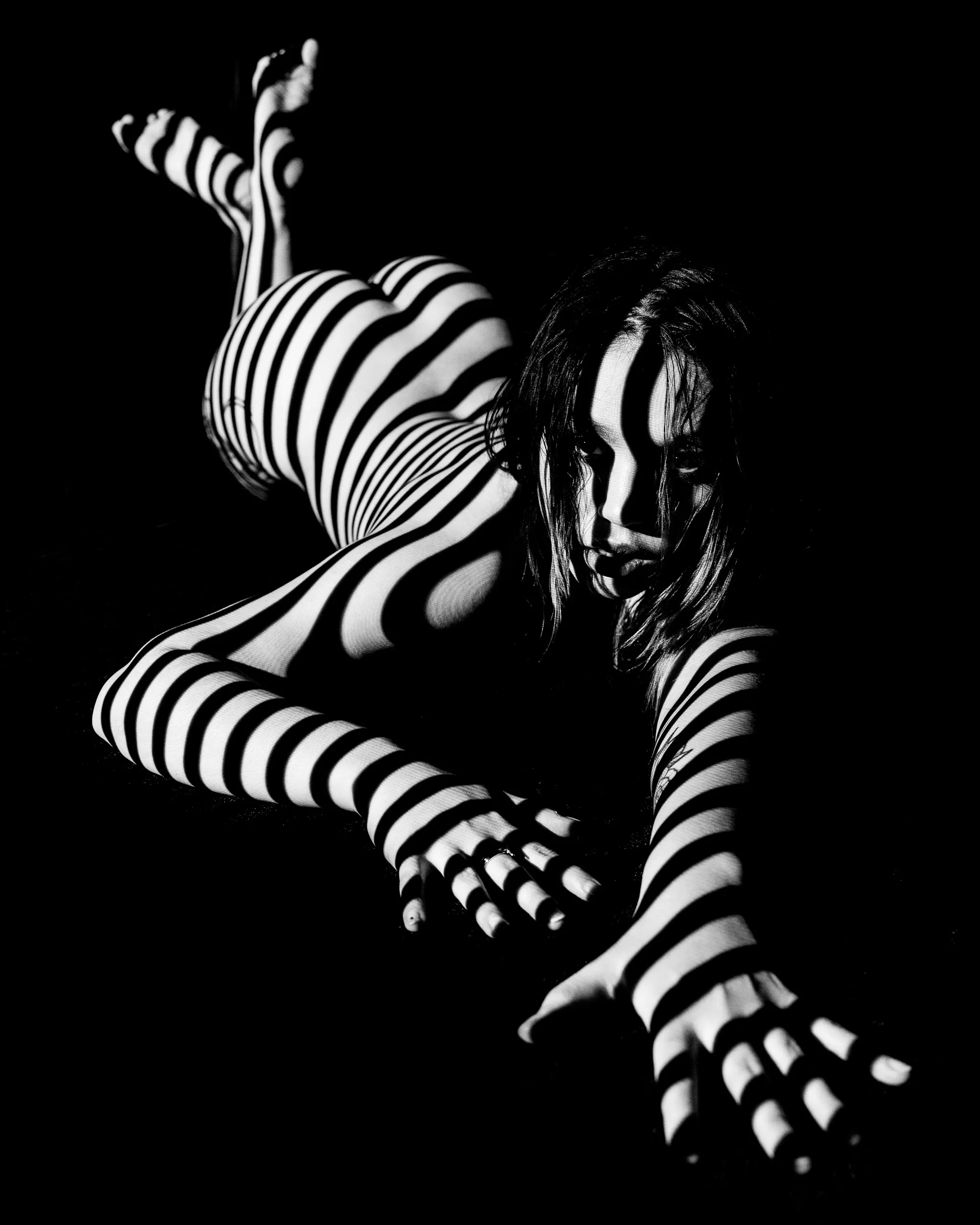 A woman crawling toward the camera, black and white lines projected onto her body.