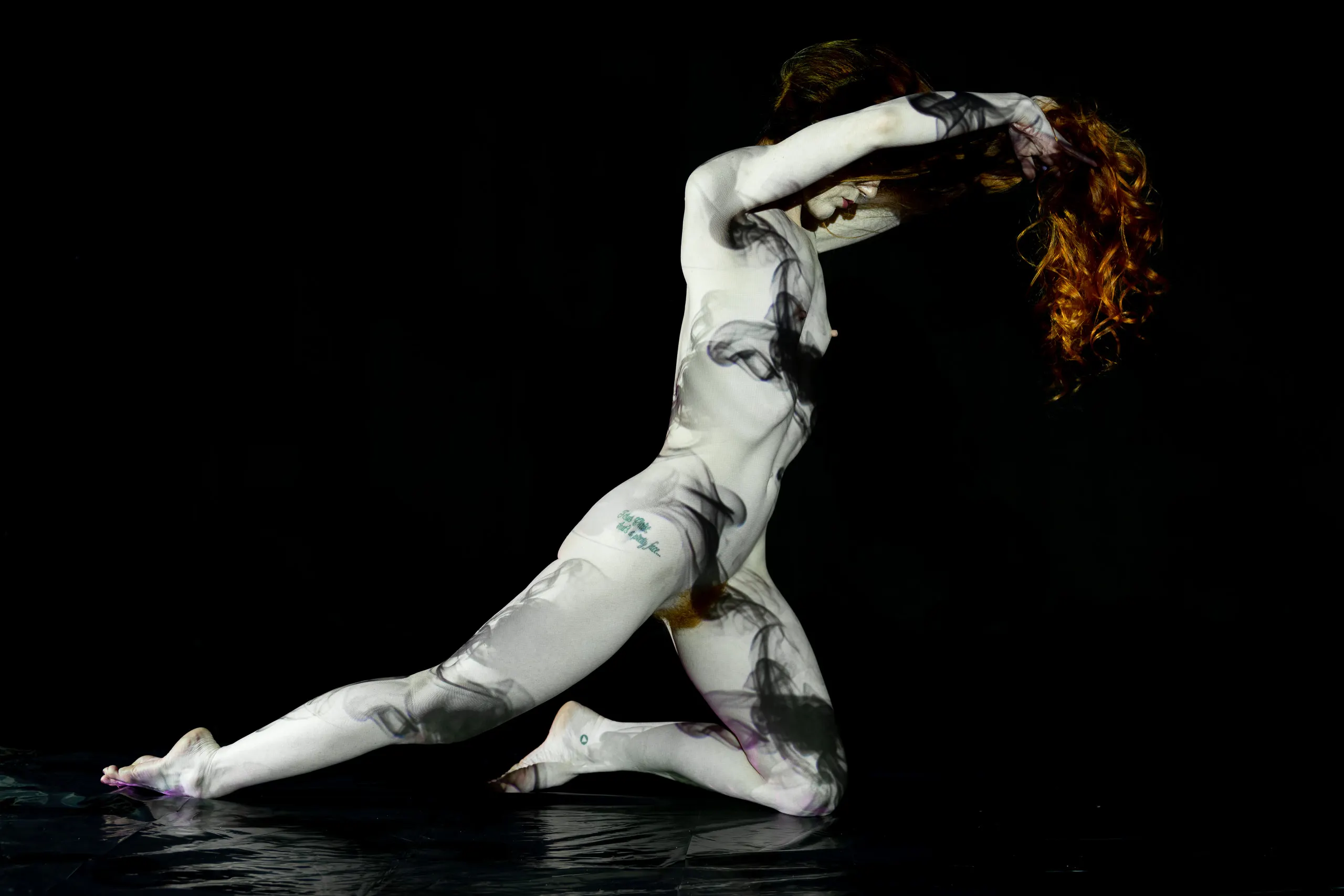 A woman kneels in profile, one arm raised to sweep her hair back, a swirling smoke-like pattern of light in black and white washing over her whole body.