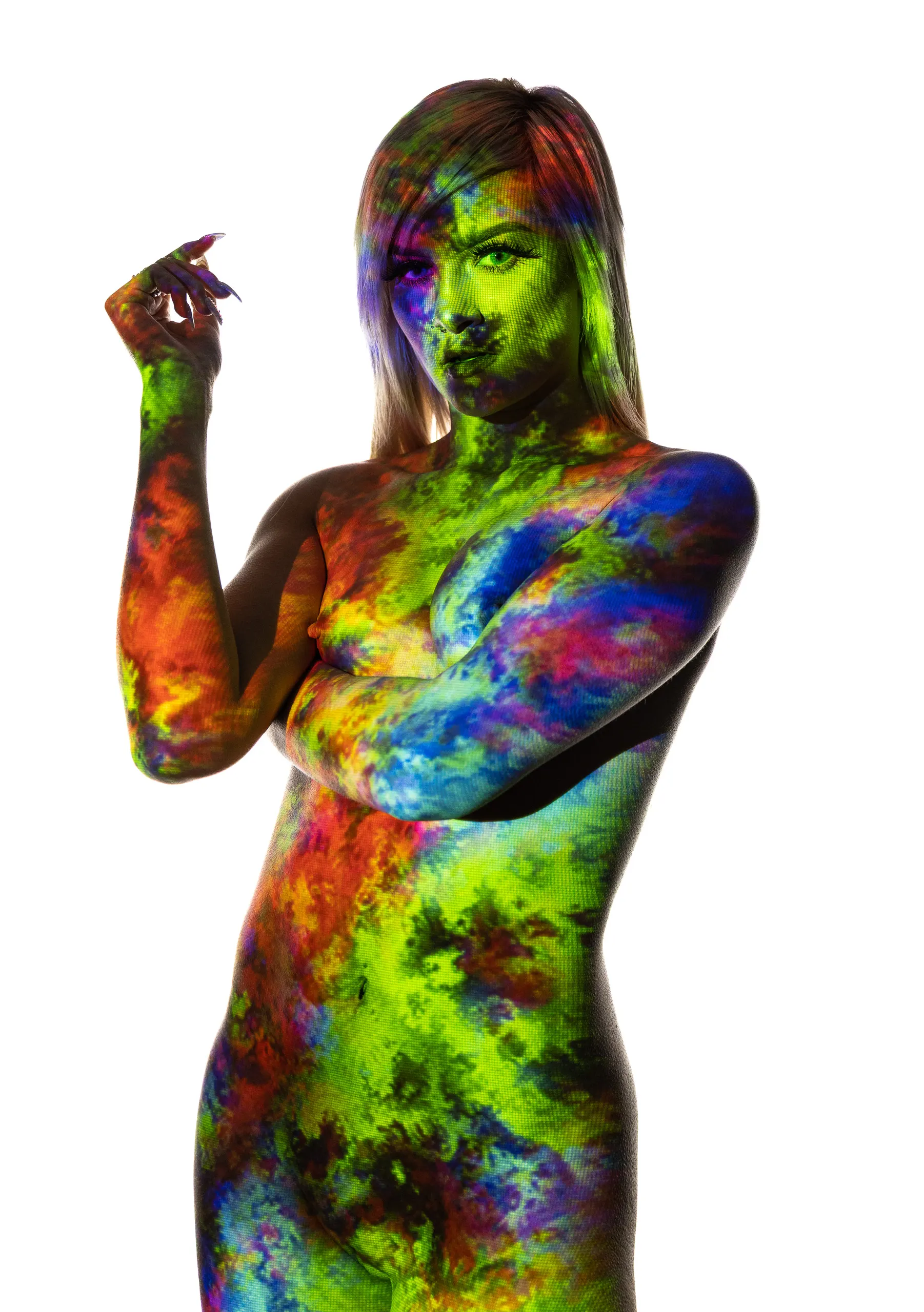 A woman stands with arms crossed over her chest, vivid green, blue, and orange cloud-like color projected across her whole body and face.