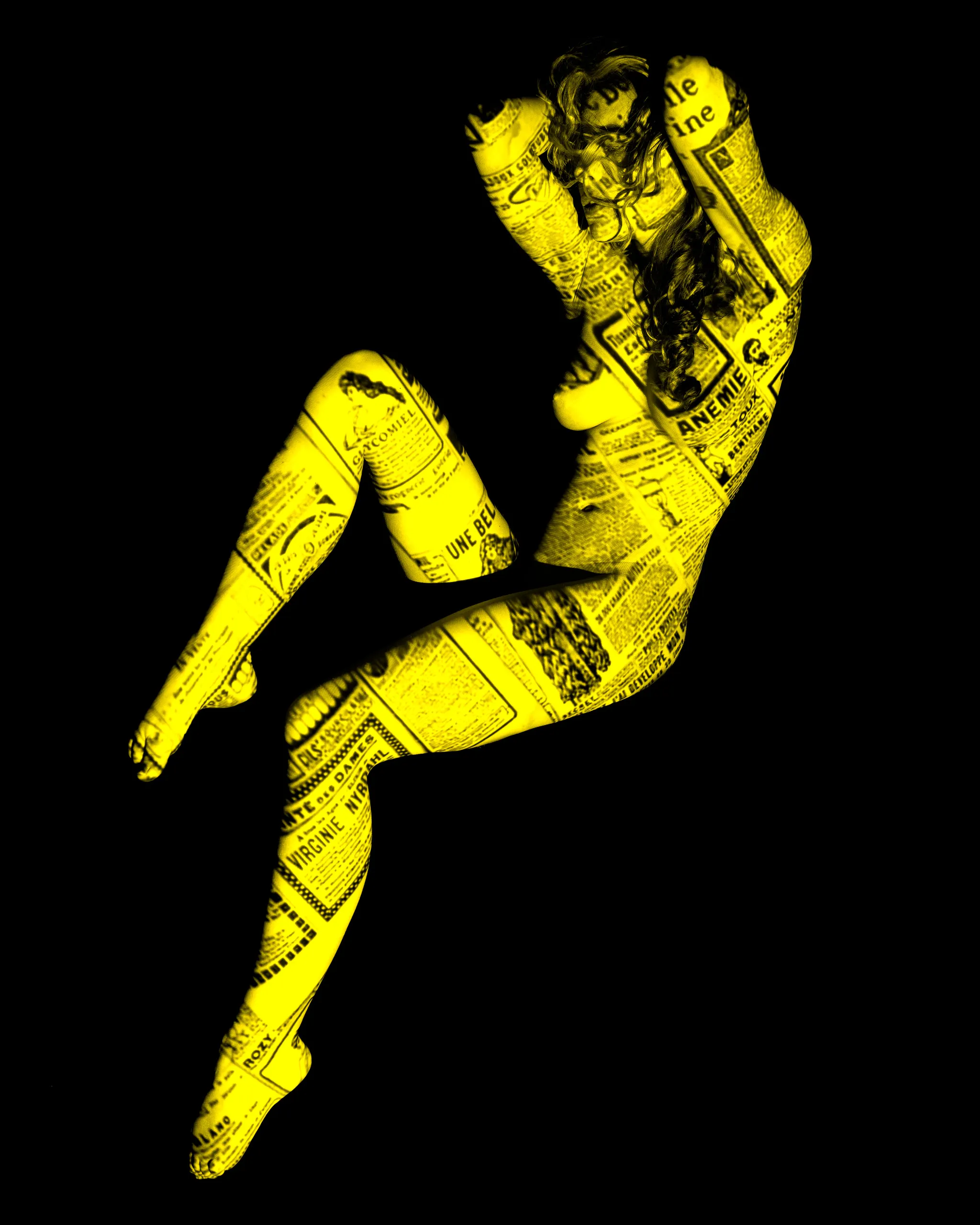 A woman sits with knees drawn up and arms crossed over her head, vintage yellow-tinted newspaper text projected across her entire body against black.