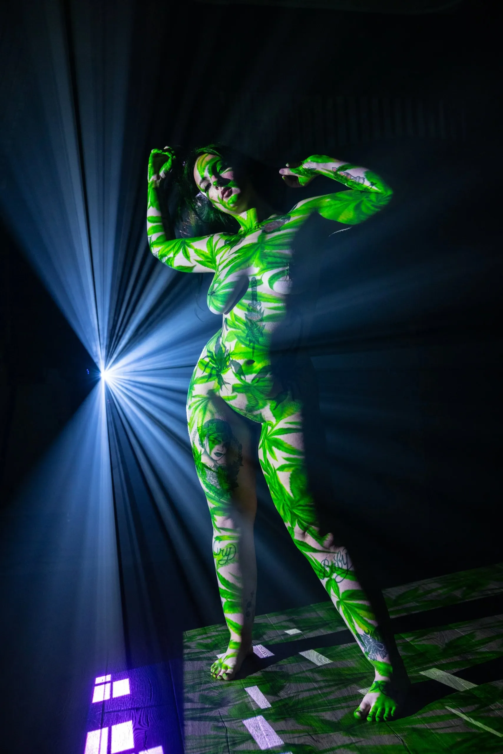 Green botanical projection covers a standing figure beside a burst of white light.