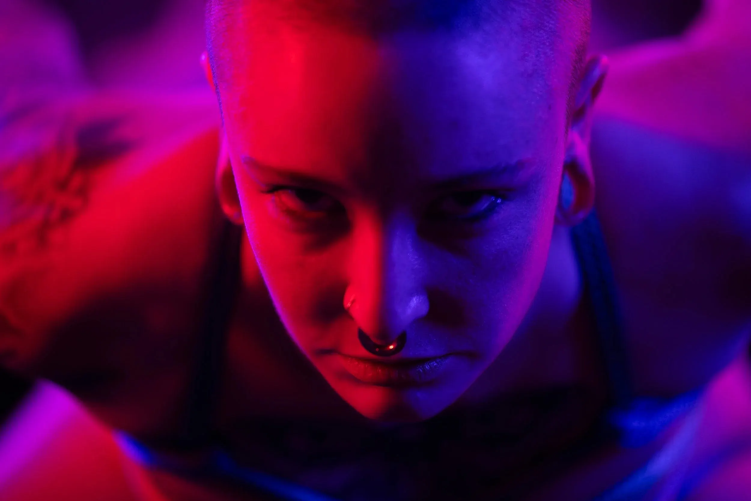 A close face looks downward through saturated red and violet light.