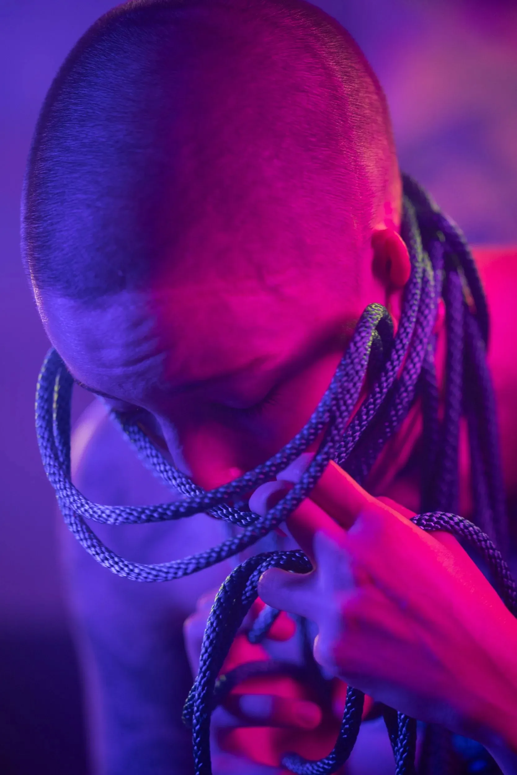 A close overhead portrait shows rope crossing a shaved head and shoulders.