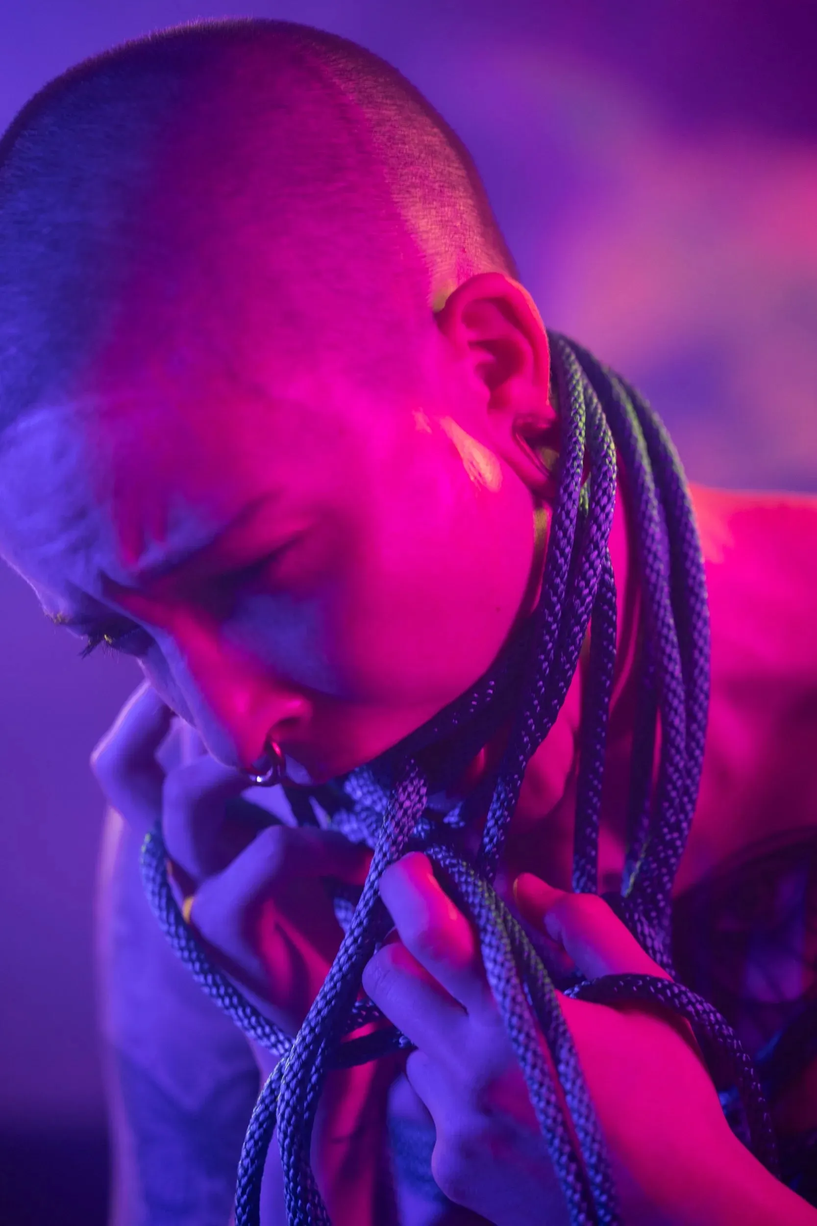 A hooded person bows their head against a soft neon background.