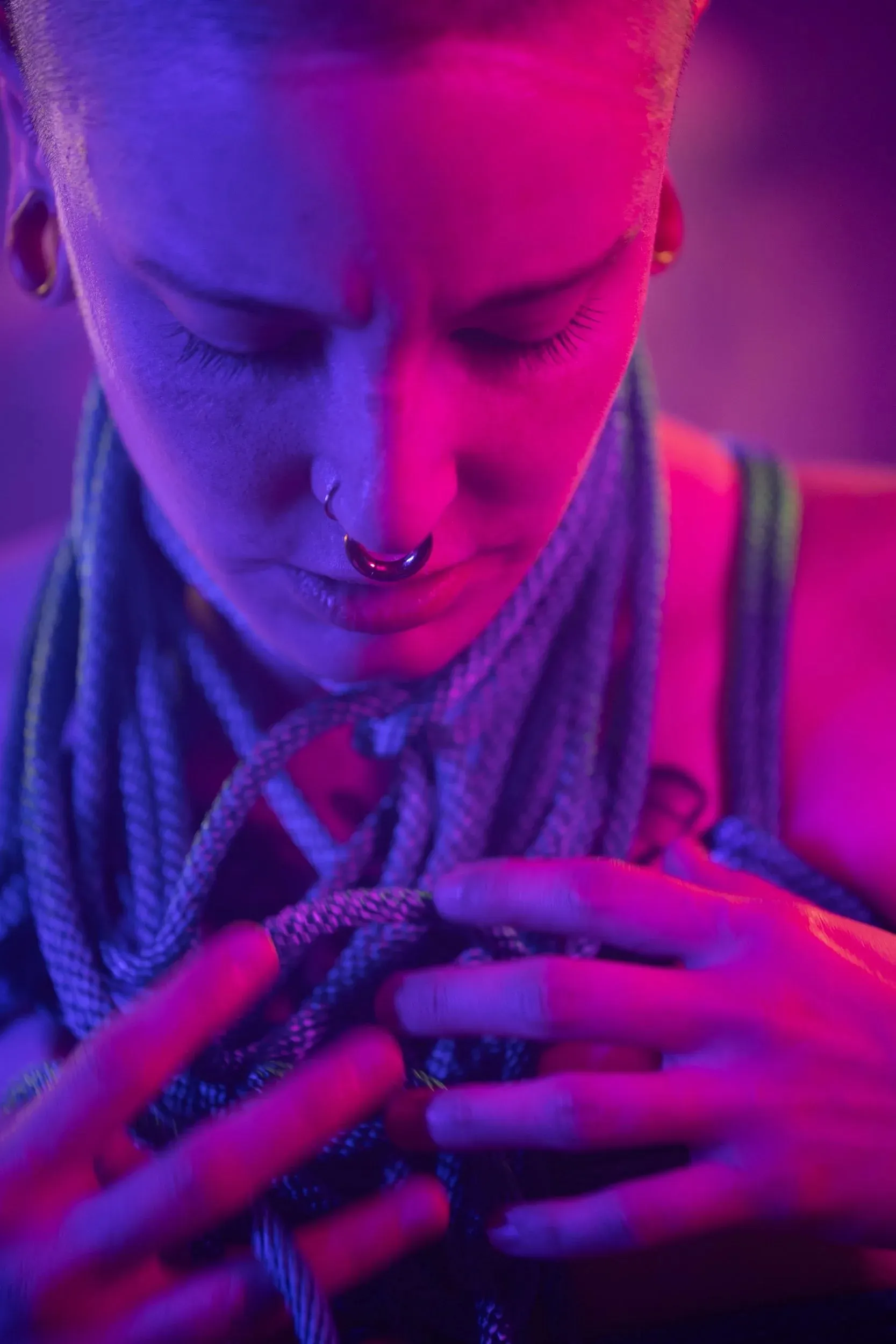 A person gathers rope at their chest under red and violet light.