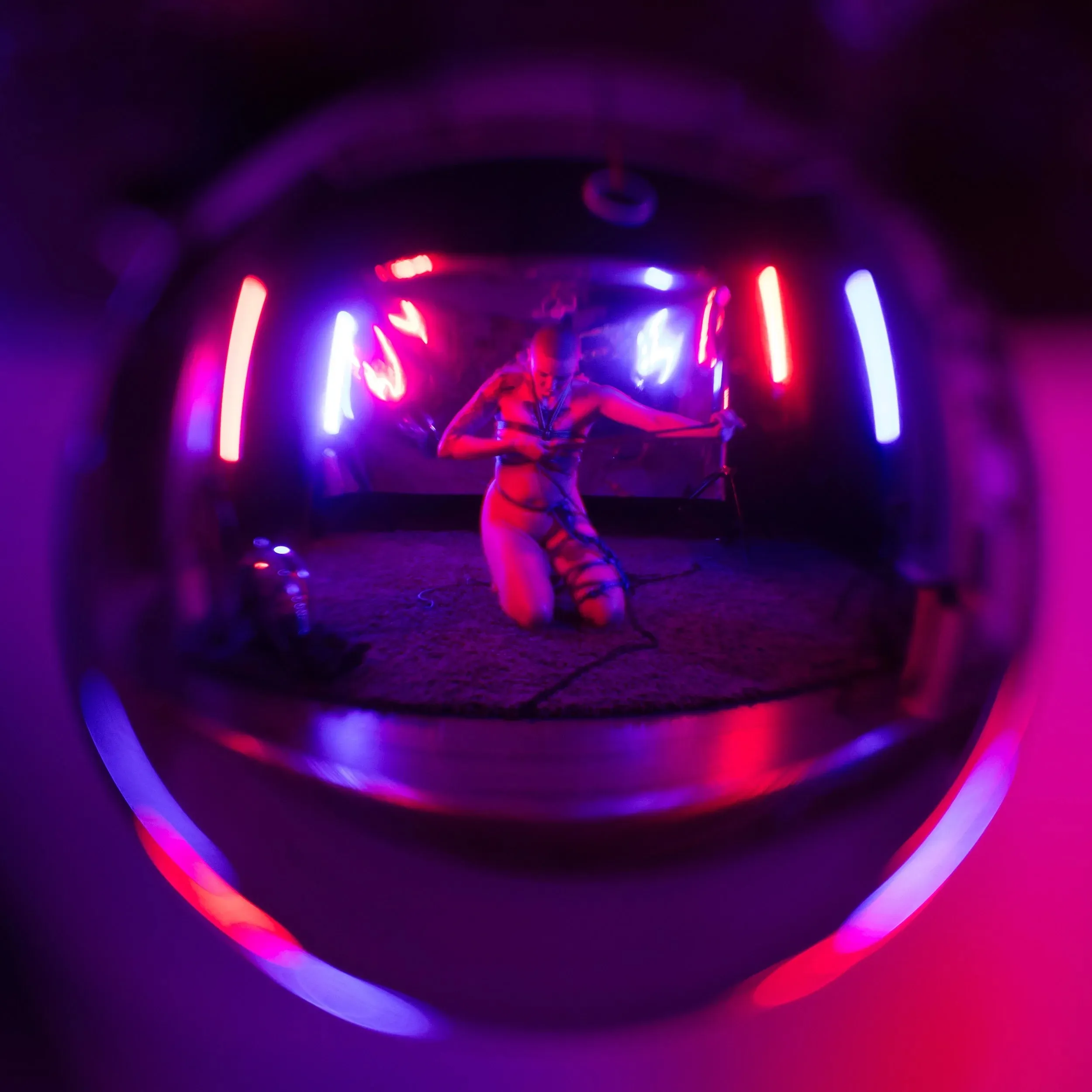 A fisheye reflection shows a small reclining figure surrounded by neon tubes.