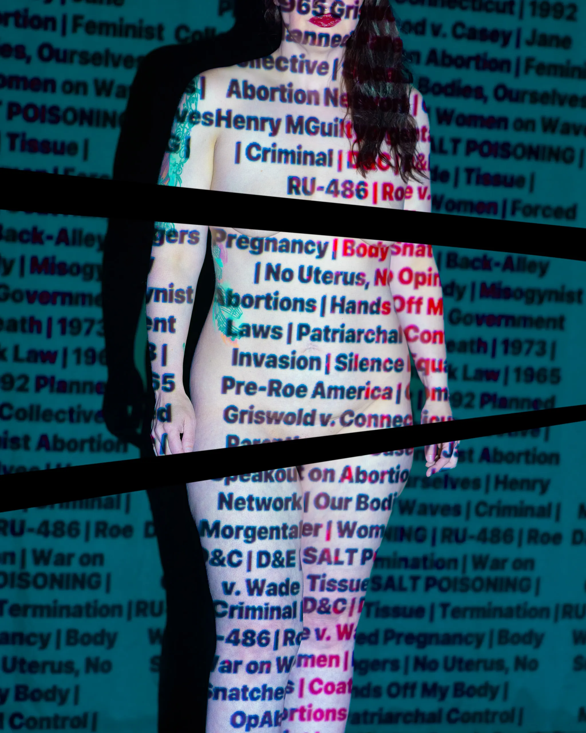 A woman stands with words about reproductive rights projected onto her body and the background.