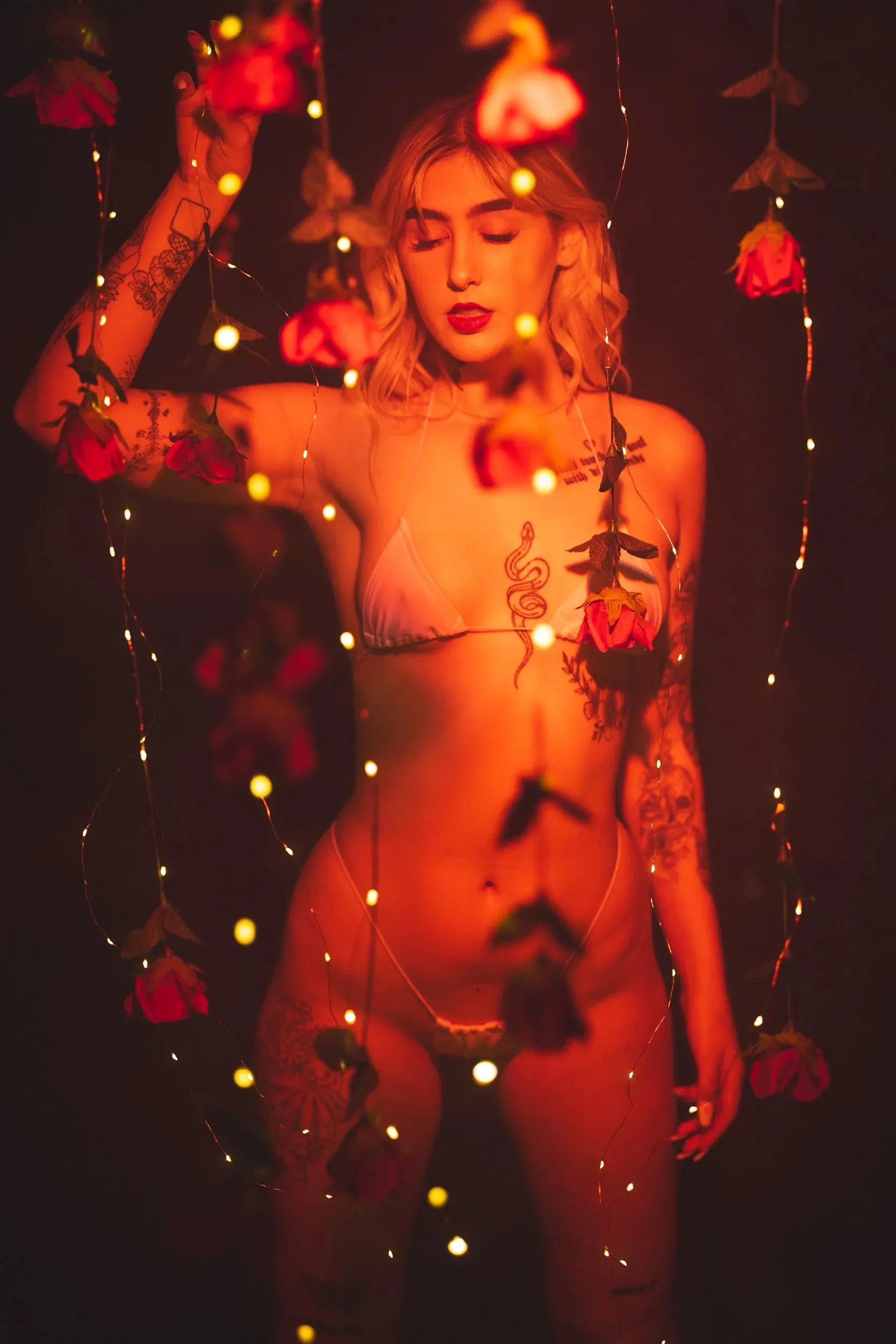 A full-length figure raises one arm beneath hanging roses.