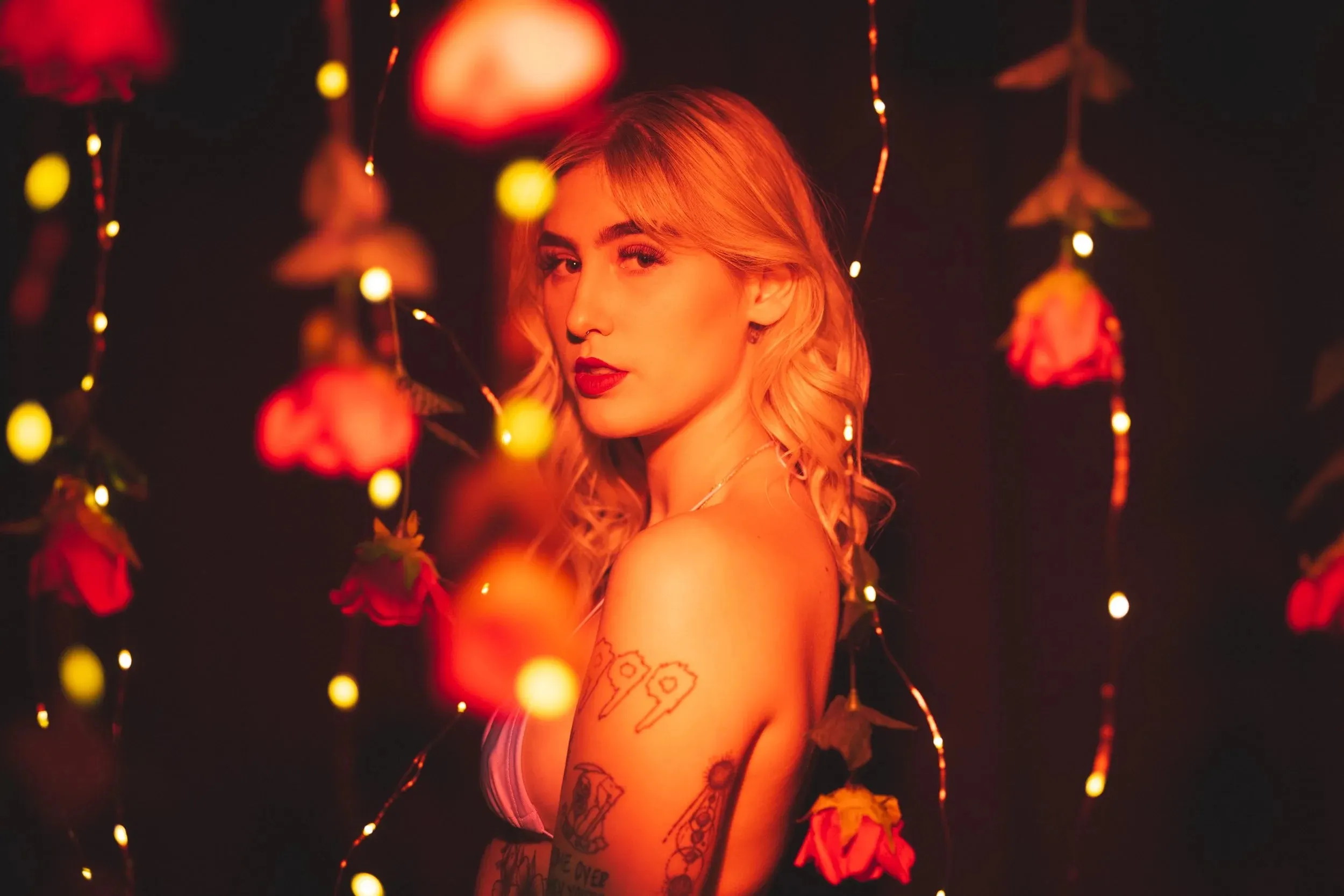 A woman looks over her shoulder through softly blurred roses and lights.