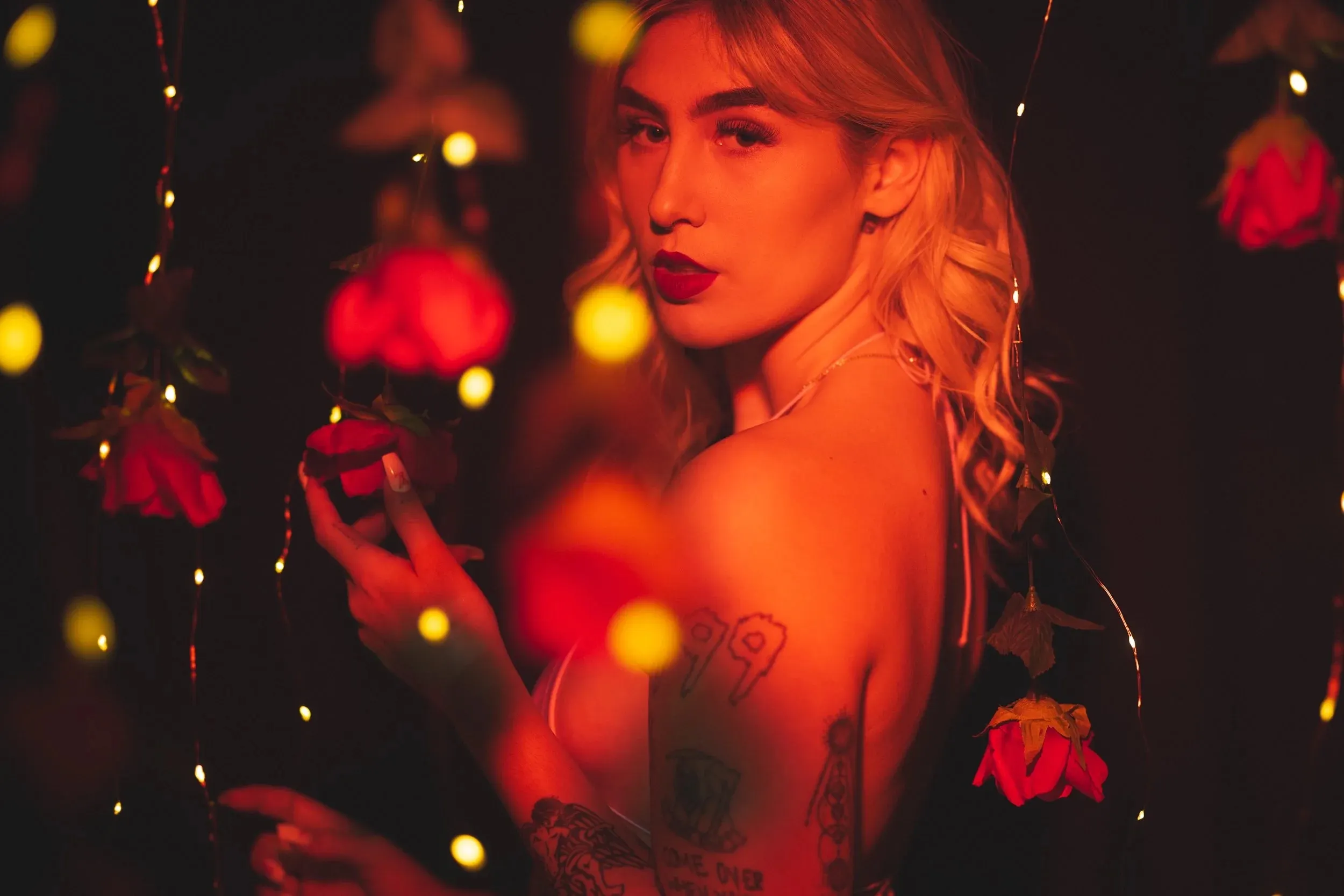 A woman turns in profile while holding a hanging red rose.
