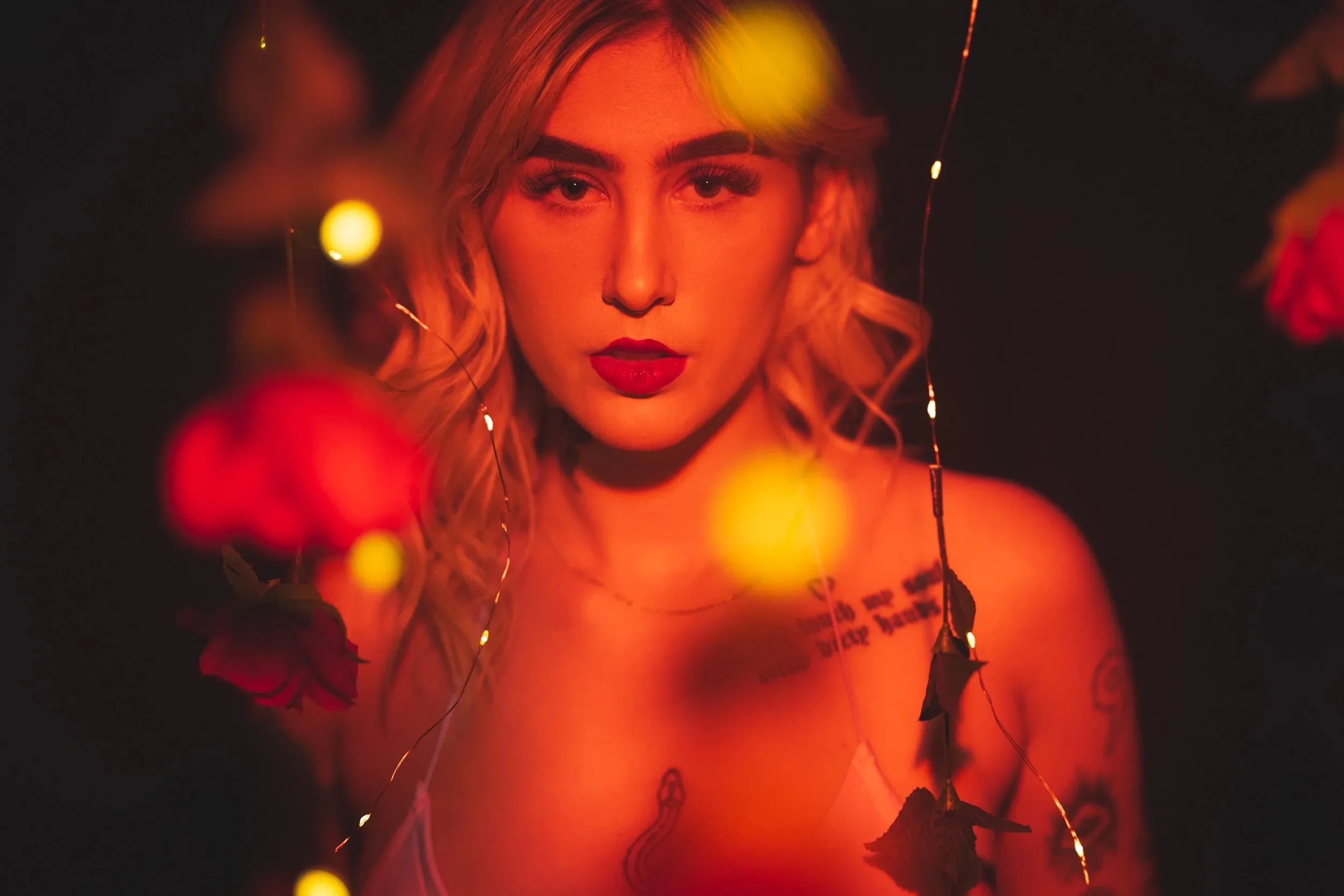 A close portrait glows orange behind out-of-focus roses and lights.