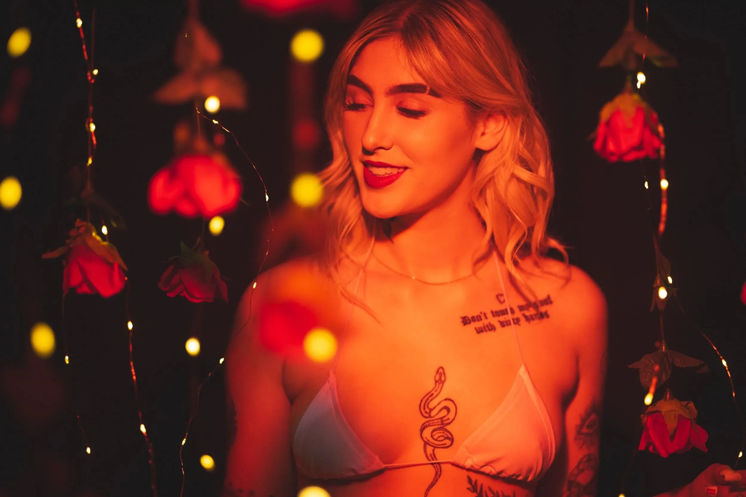 A smiling woman looks down among suspended red roses.
