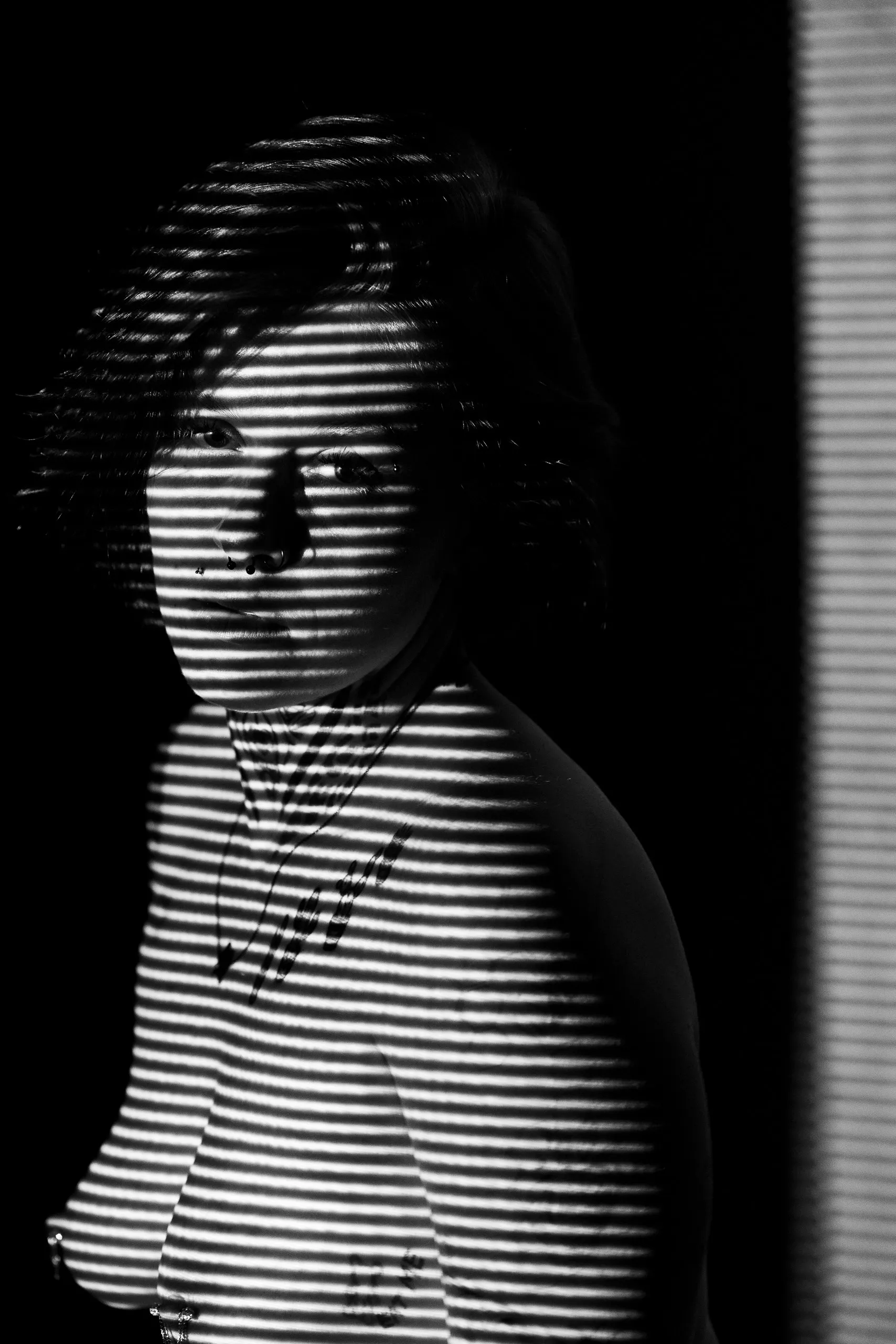 A woman looks toward the camera over her shoulder, horizontal lines of light falling across her face and chest.