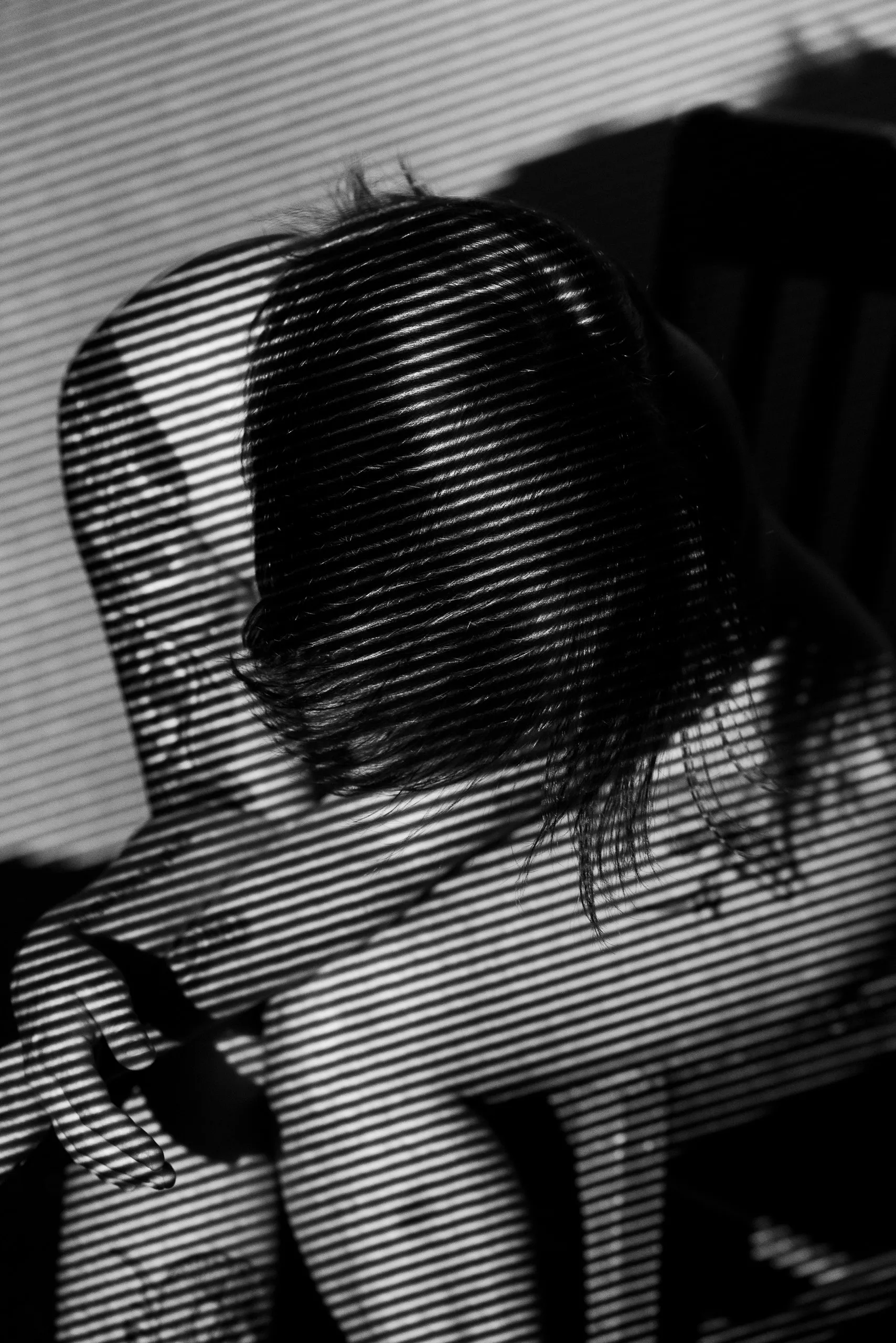 A seated figure bows her head toward her thigh, her hair and arms covered in fine diagonal lines of light.