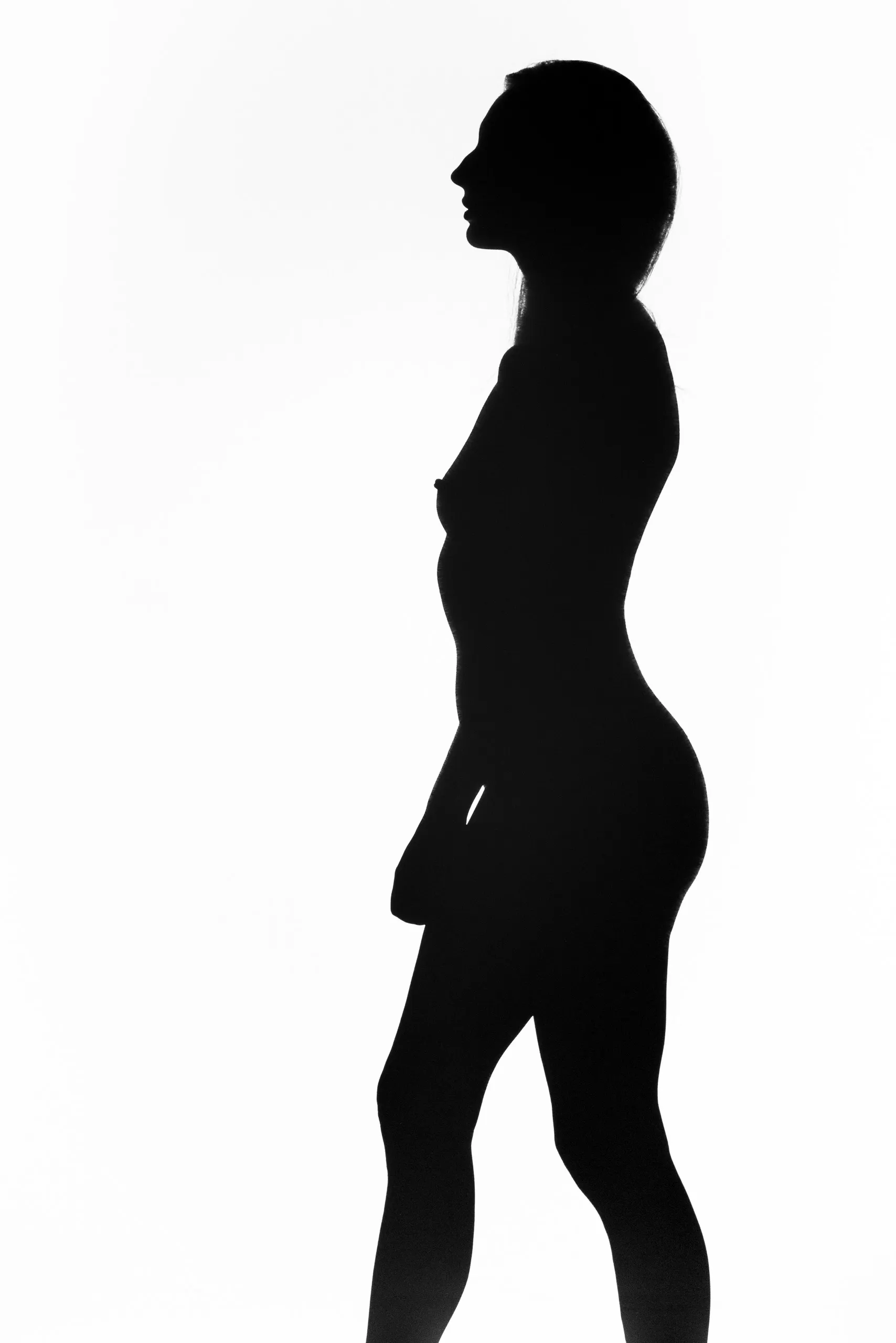 A woman stands in full profile as a solid black silhouette against a bright white ground, chin lifted, hair drawn back, one leg carried forward mid-stride.