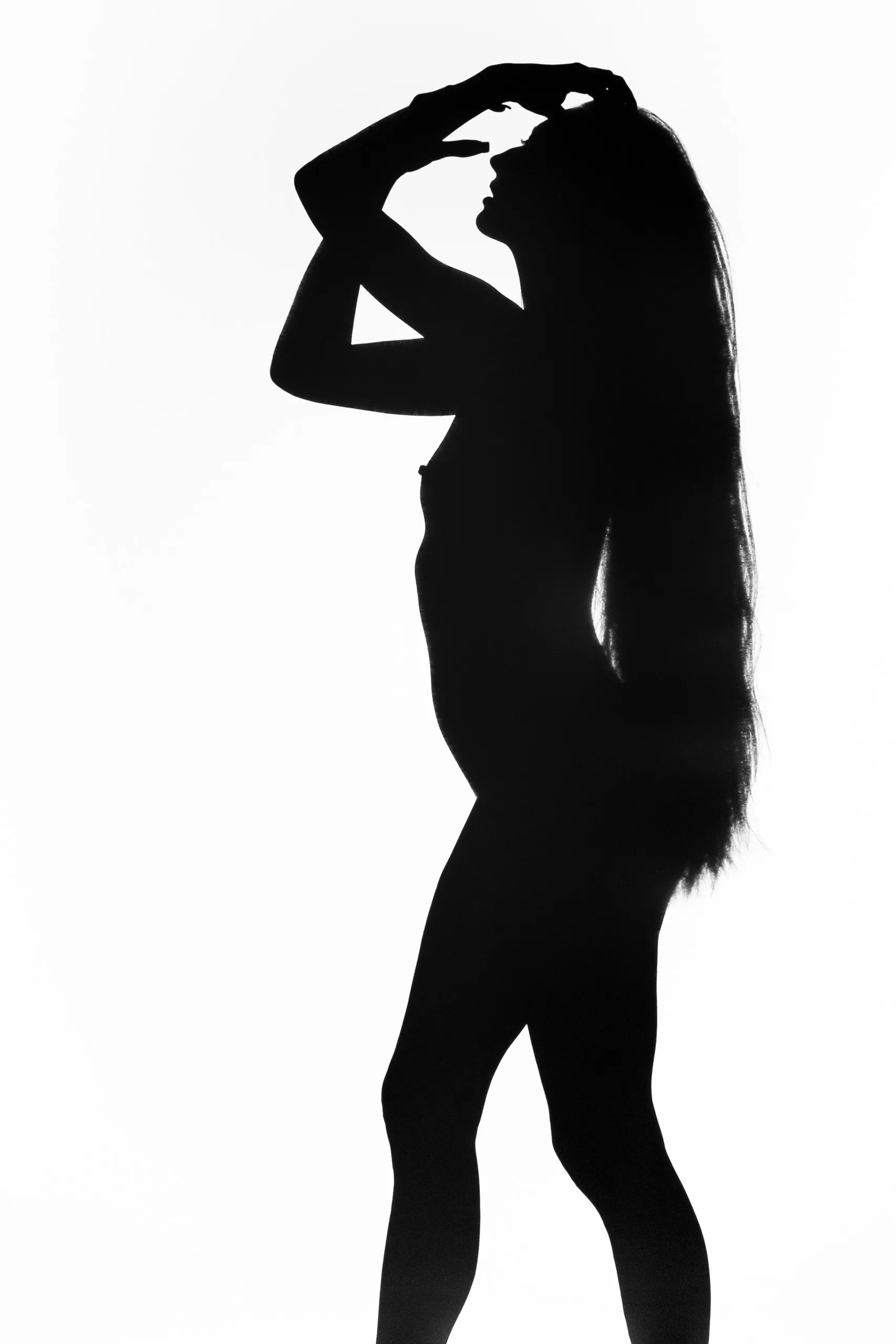 A silhouetted woman raises both arms to meet above her head and tilts her face upward, very long hair falling in a lit curtain down her back.