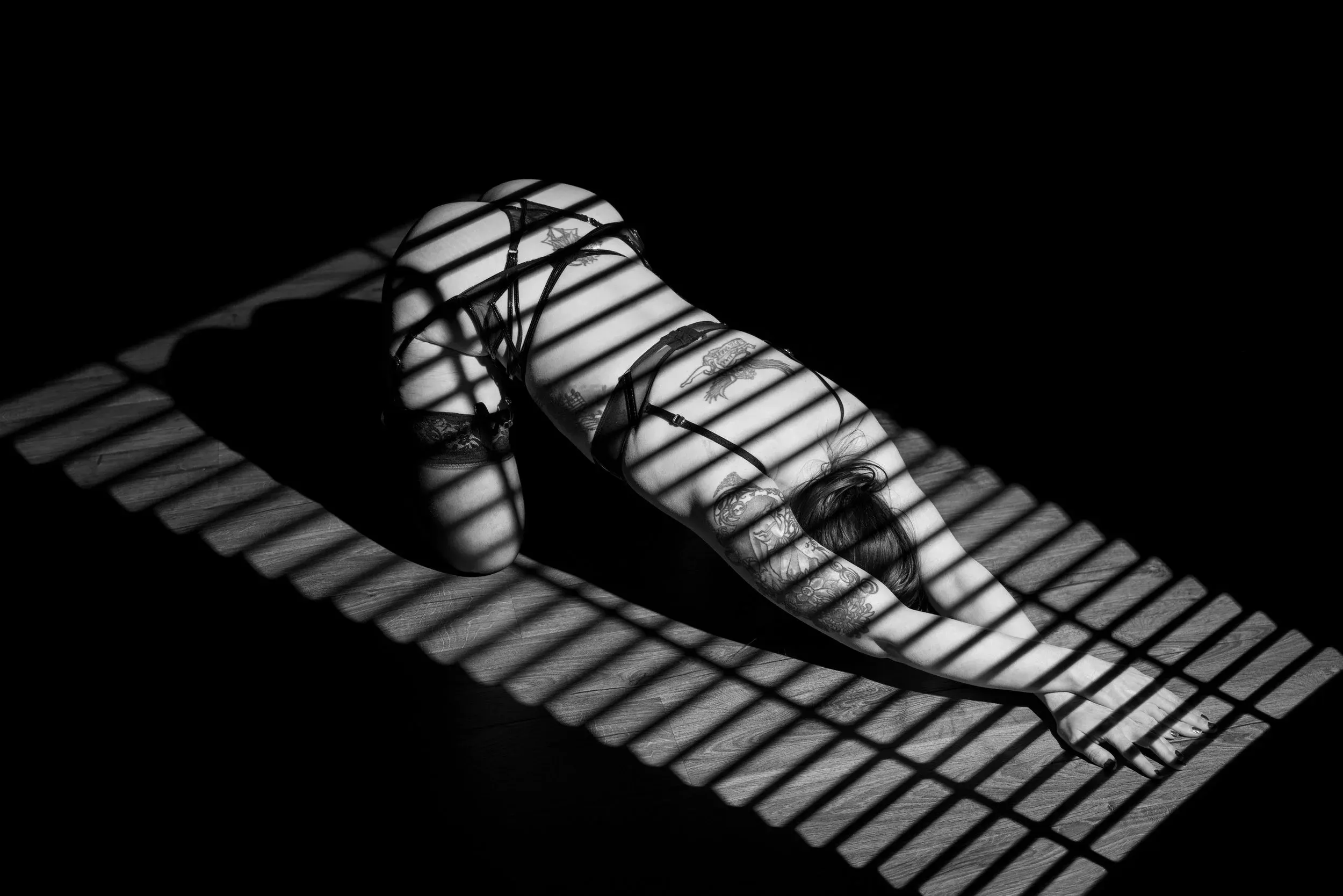 Striped window light crosses a bowing woman in black and white.